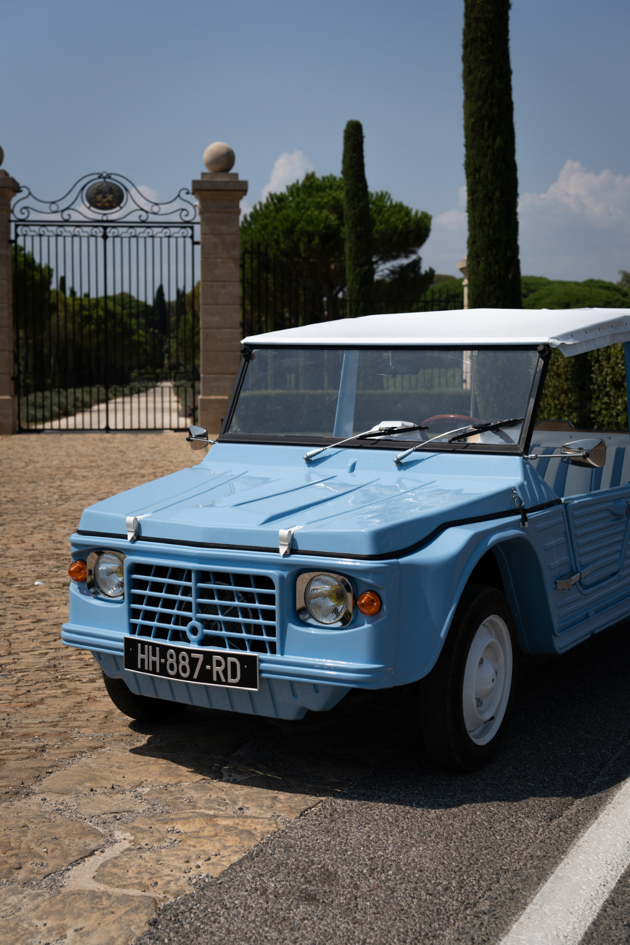 Blue Citroën Méhari with white soft top in front of a private estate gate