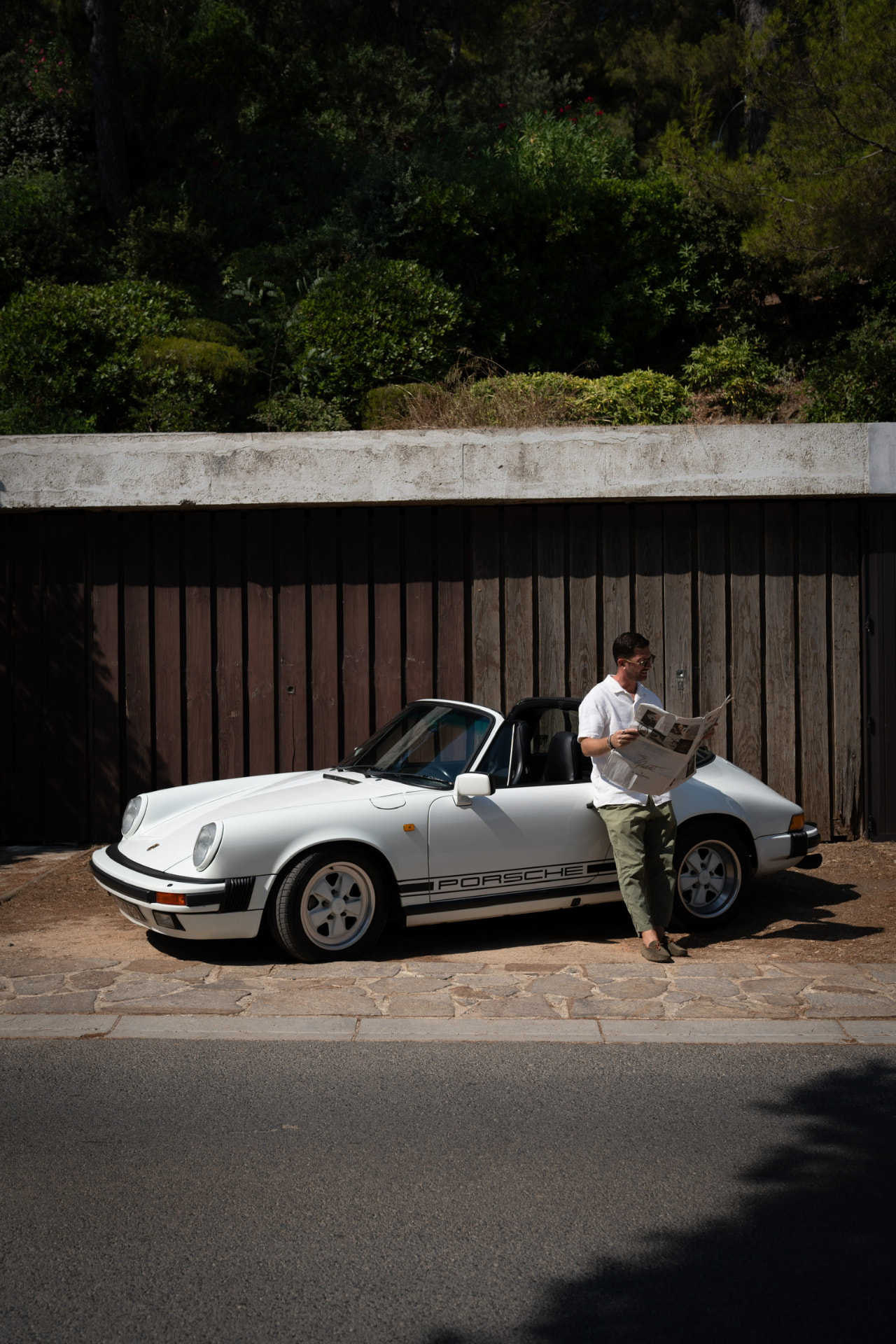 Man reading a newspaper leaning on a white Porsche 911 Targa during a photo shoot